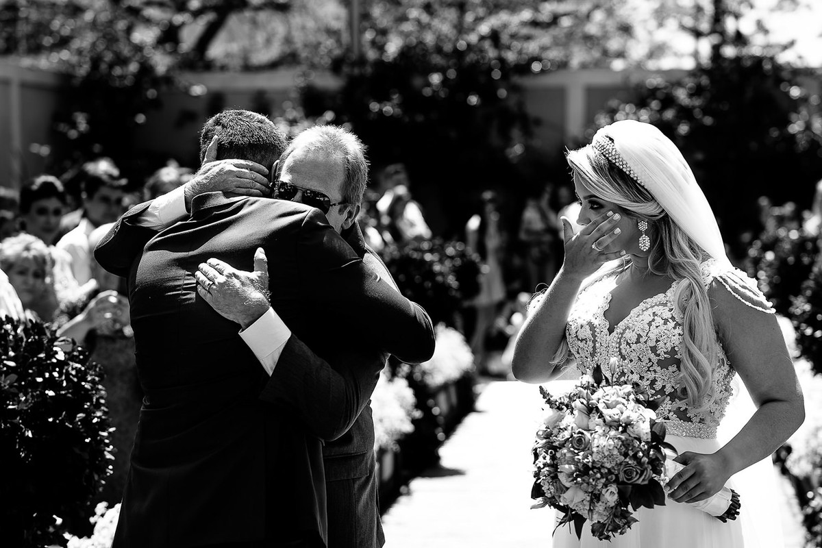 Foto de noiva emocionada ao ver pai abraçando noivo