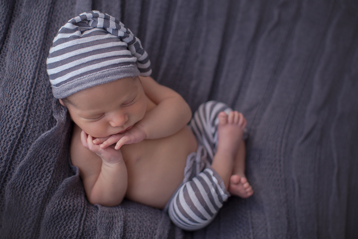  Foto feita na casa do cliente em Curitiba. Book Newborn do Theo com Gustavo Sousa. Pose de perninhas cruzadas de barriguinha para cima. Roupa de pijama. Mãos apoinado a cabecinha.