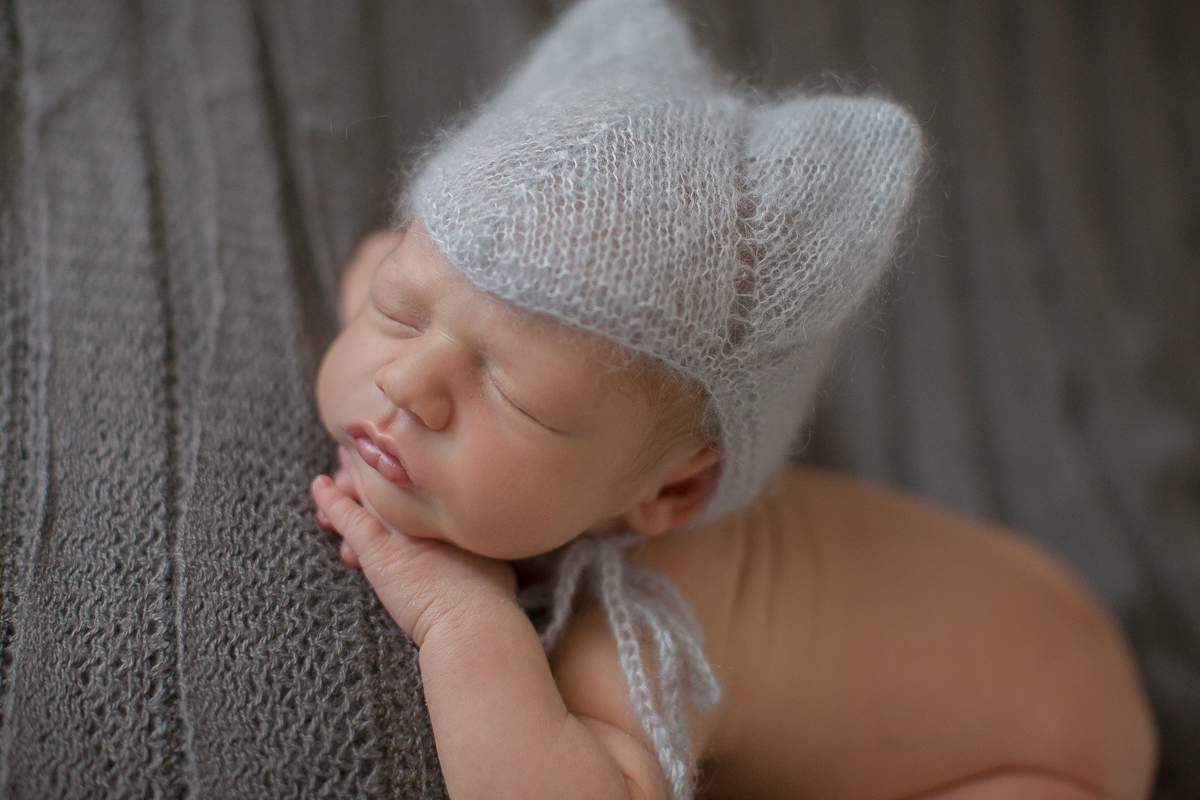  Foto feita no estúdio Gustavo Sousa Newborn em Curitiba. Book do Theo. Sessão de fotos. Touquinha. Deitado na pose do bracinho na manta cinza.