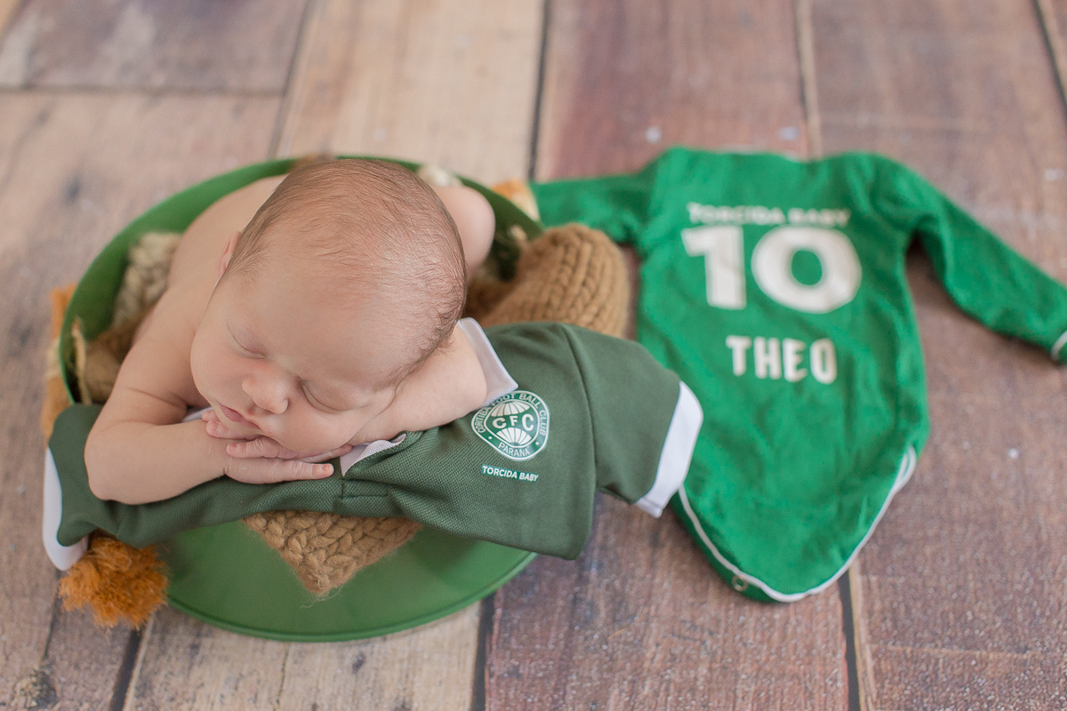  Foto feita no estúdio Gustavo Sousa Newborn em Curitiba. Book do Theo. Sessão de fotos. Pose de bracinho apoiado na camiseta de futebol. Fundo de madeira