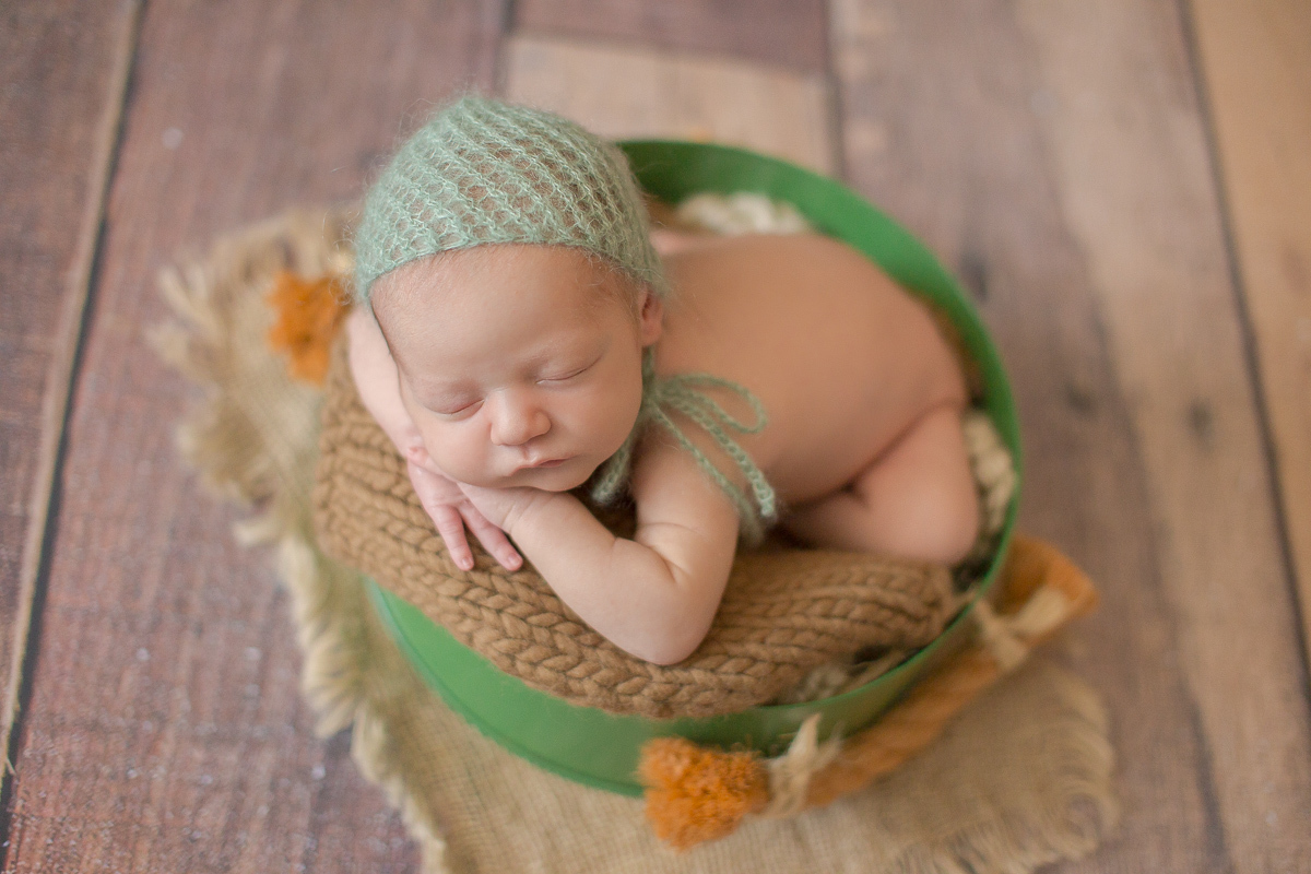  Foto feita no estúdio Gustavo Sousa Newborn em Curitiba. Book do Theo. Sessão de fotos. Pose de bracinho com touca verde água. Dentro de baldinho verde. Fundo de madeira