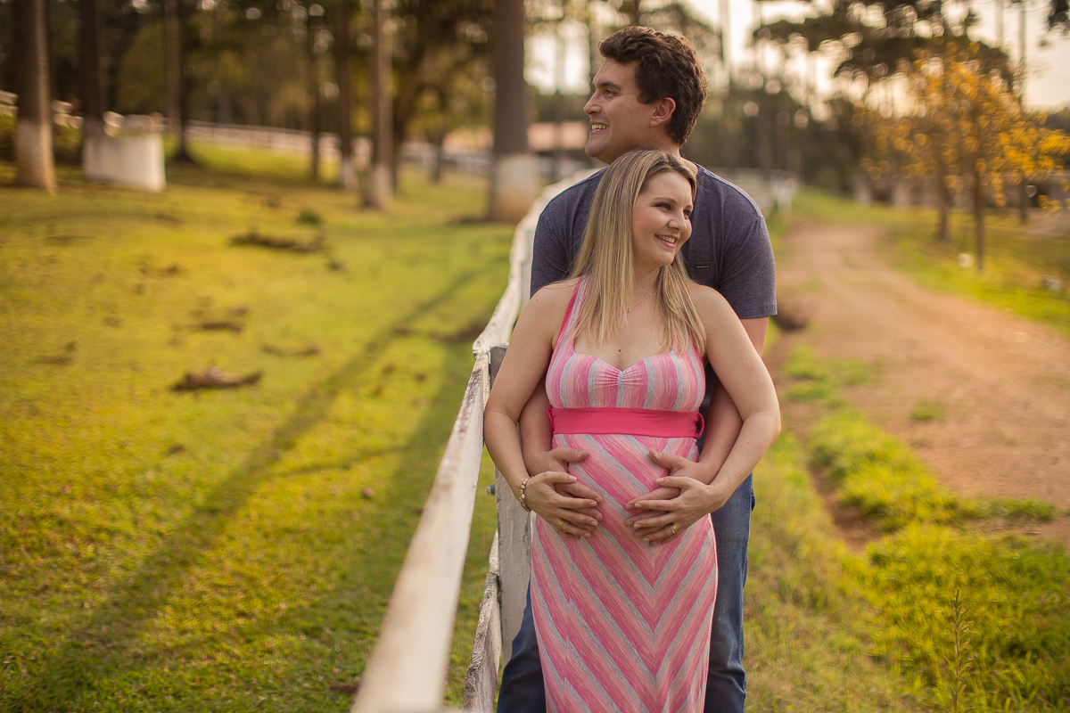 Ensaio gestante da Pamela e Fabio com Gustavo Sousa fotografia em Curitiba. Book em externa em haras. Gravida com vestido listrado rosa e cinza.  ao lado da cerca. 