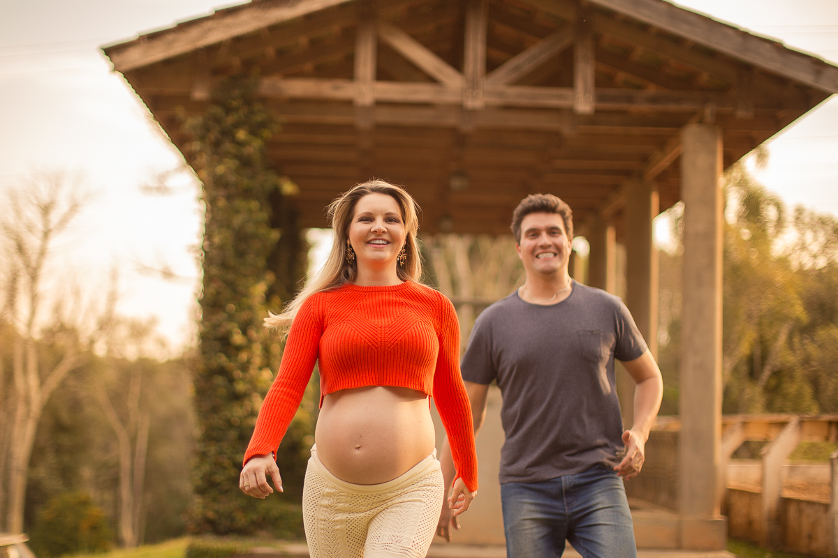 Ensaio gestante da Pamela e Fabio com Gustavo Sousa fotografia em Curitiba. Book em externa em haras. Gravida com calça amarela e blusa laranjada. Pose na capela