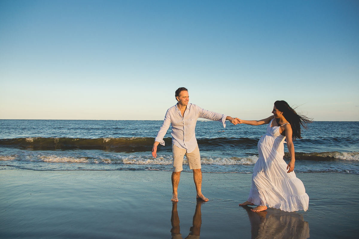 ensaio gestante em externa feito em curitiba com Gustavo Sousa Fotografia. Foto na praia com gestante no colo. por do sol. mãos dadas. vestido branco