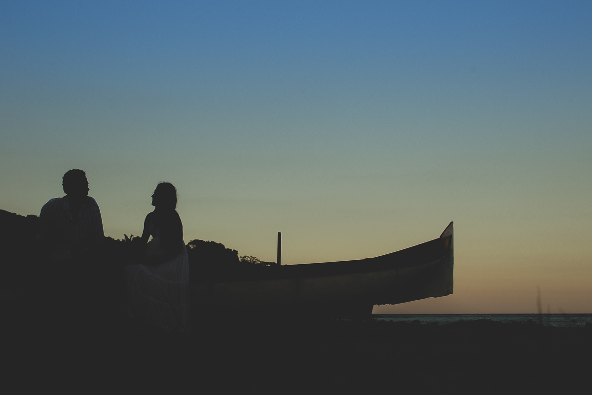 ensaio gestante em externa feito em curitiba com Gustavo Sousa Fotografia. Foto na praia com gestante no colo. por do sol. cilhueta com barco