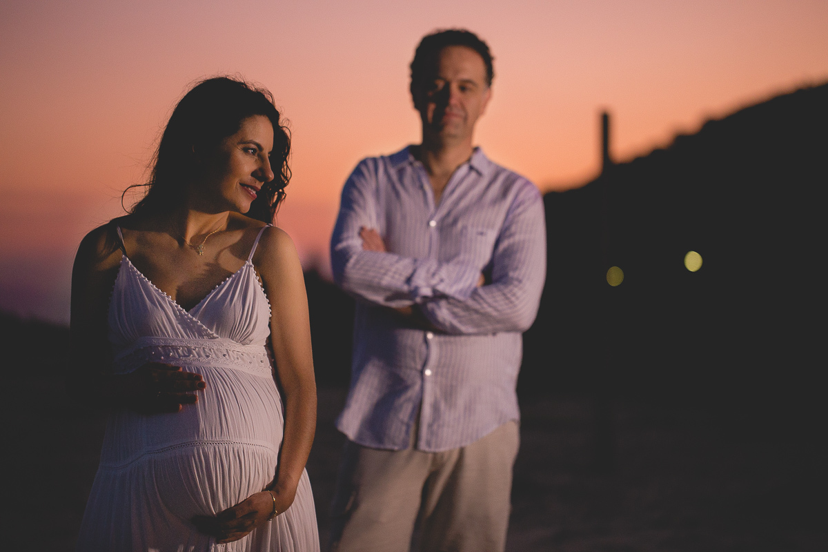 ensaio gestante em externa feito em curitiba com Gustavo Sousa Fotografia. Foto na praia com gestante no colo. por do sol. gravida na frente e esposo atrás