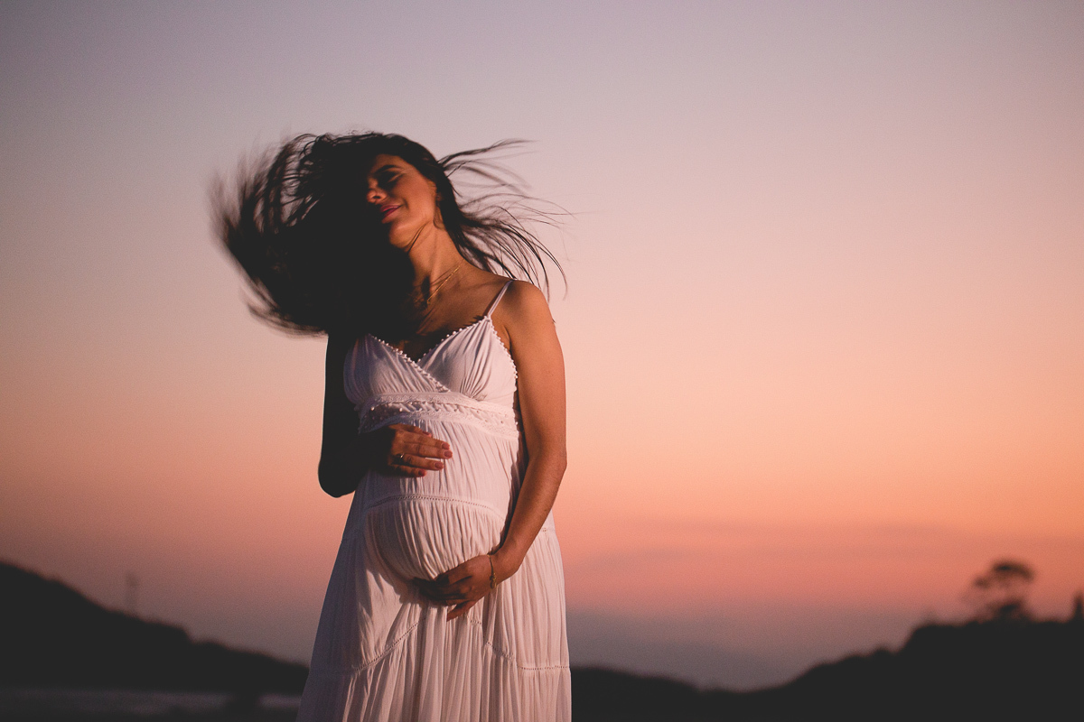 ensaio gestante em externa feito em curitiba com Gustavo Sousa Fotografia. Foto na praia com gestante no colo. por do sol. cabelo voando.