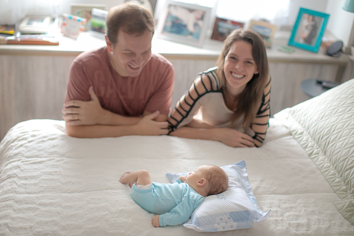 Foto feita na casa do cliente Newborn  lifestyle em Curitiba. Book do Nicolas. No quarto dos pais. Newborn na cama dos pais. Pai e mãe sorrindo ao fundo.