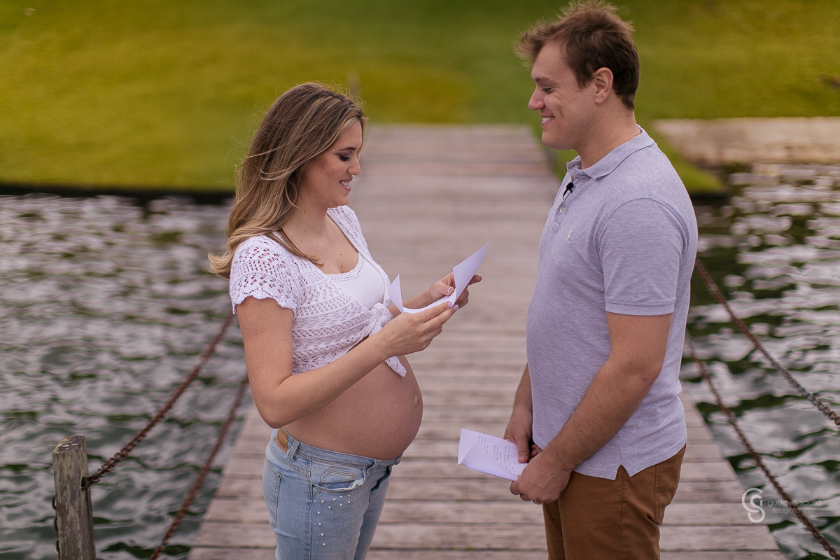 Ensaio gestante da Paty e Jo no estúdio Gustavo Sousa fotografia em Curitiba. Book em externa. Vestido florido Local Laggus Residencial Náutico Mãos na barriga . Gustavo Sousa Fotografia. Lendo carta no deck de madeira em um lago