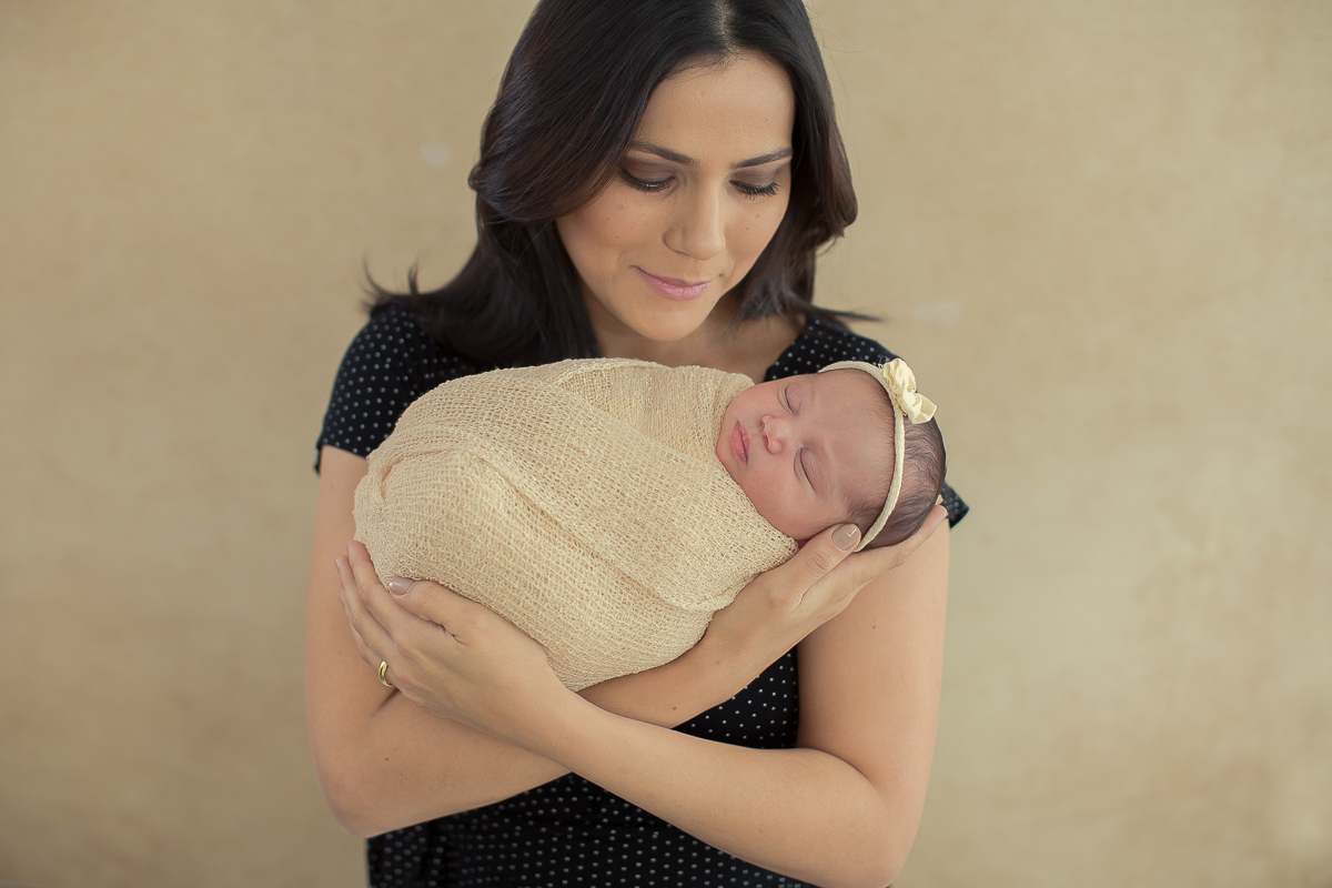 Ensaio newborn em Curitiba. Book feito  em produção cleam. Gustavo Sousa e Kátia Hille. Pose Básica. Fundo rosa. Manta Pipoca, roupa bege. Fundo beje. mãe vestidade de preto. Olha para a bebê