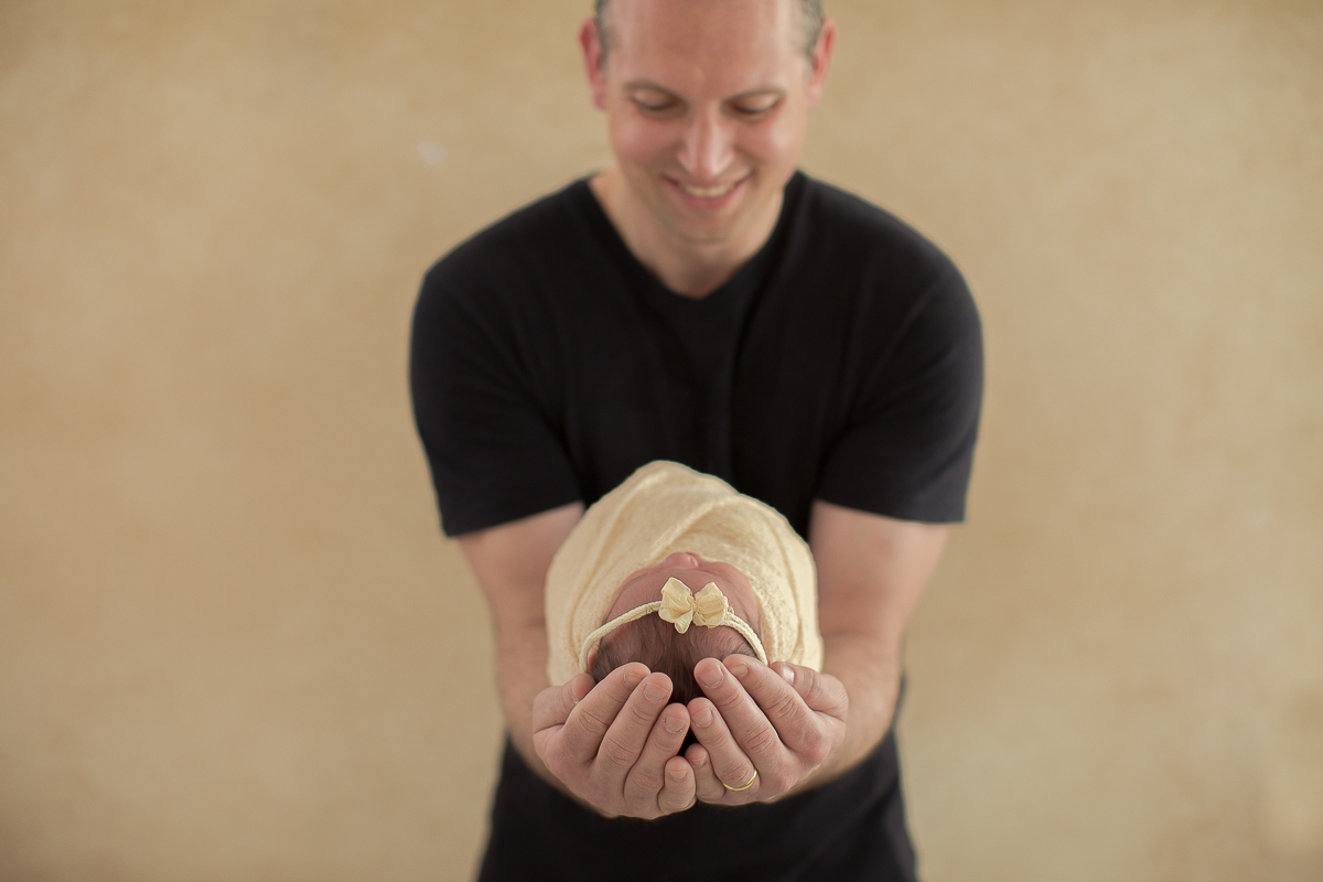 Ensaio newborn em Curitiba. Book feito  em produção cleam. Gustavo Sousa e Kátia Hille. Pose Básica. Fundo rosa. Manta Pipoca, roupa bege. Fundo beje. pai vestido de preto. Olha para a bebê