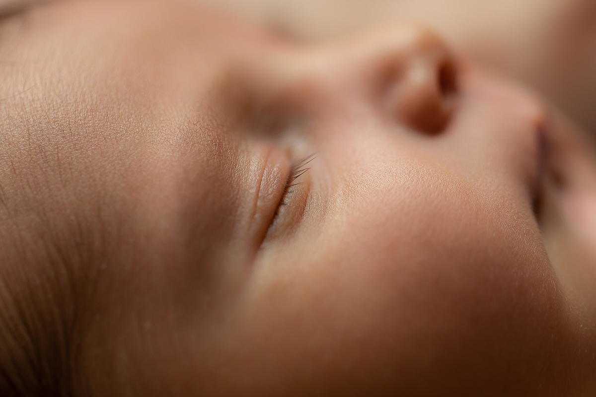 Ensaio Newborn do Theo feito no estúdio Gustavo Sousa fotografia em Curitiba. Fundo de madeira. Enrolado no wrap azul. Pelo e, volta do acessório de crochet. Pose barriga para cima. Fundo de madeira. Detalhe olho..