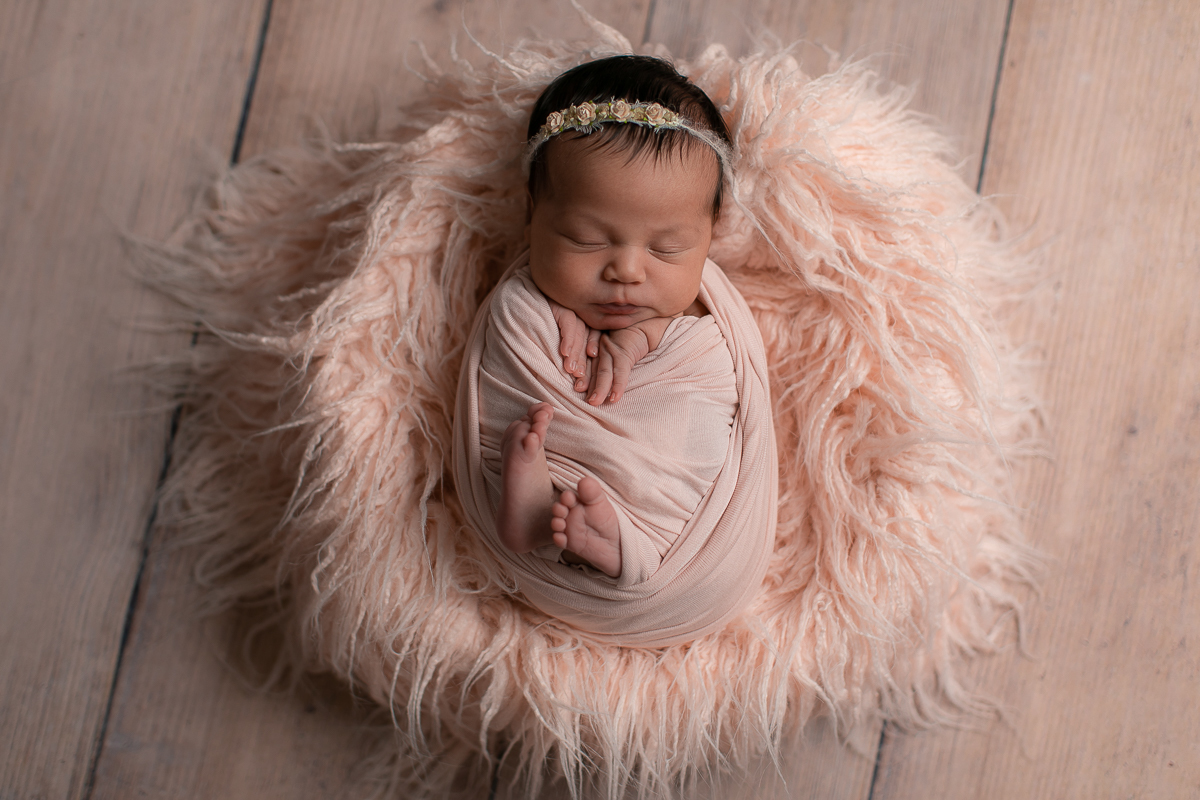 Ensaio Newborn da Maitê feita no estúdio Gustavo Sousa fotografia em Curitiba.  Foto feita cheia de amor, segurança e carinho. Produção simples e Clean. Fundo de madeira. Tons Rosa e bege. Enrolada no Wrap rosa. Pés de fora
