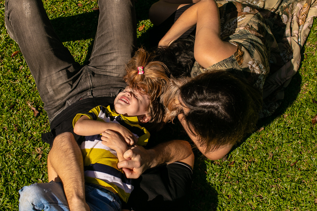 Gustavo Sousa fotografia em ensaio família e gestante na fazenda e haras perto de Curitiba. família brincando na grama deitados. Com a cachorrinha