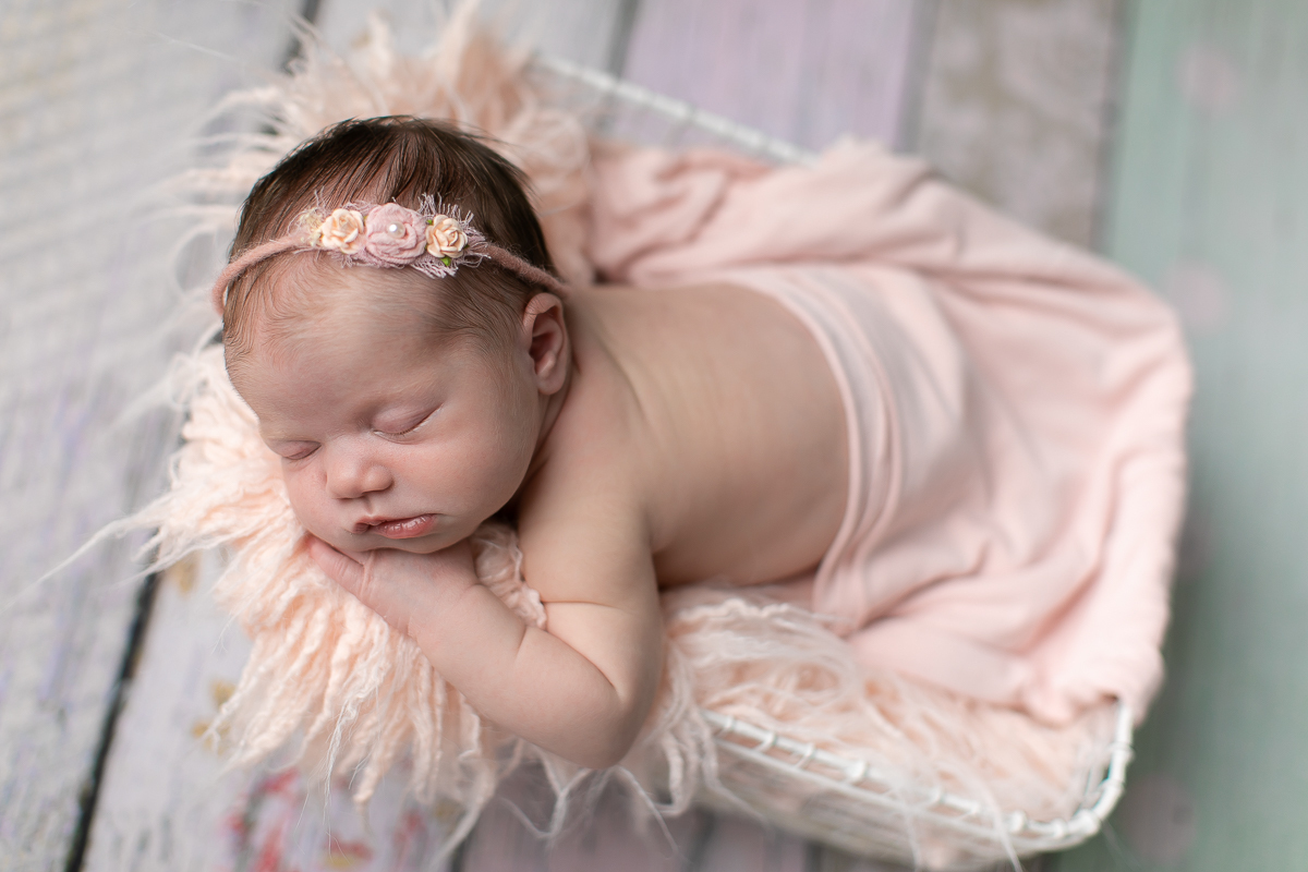 Ensaio newborn da sophia no estúdio gustavo sousa fotografia em curitiba produção simples e clean.  Cesto prop aramado brando utilizado na produção com pelo rosa e utilização de wrap tecido cor de rosa. Pose do bracinho. Uso de headband com flores enfeite
