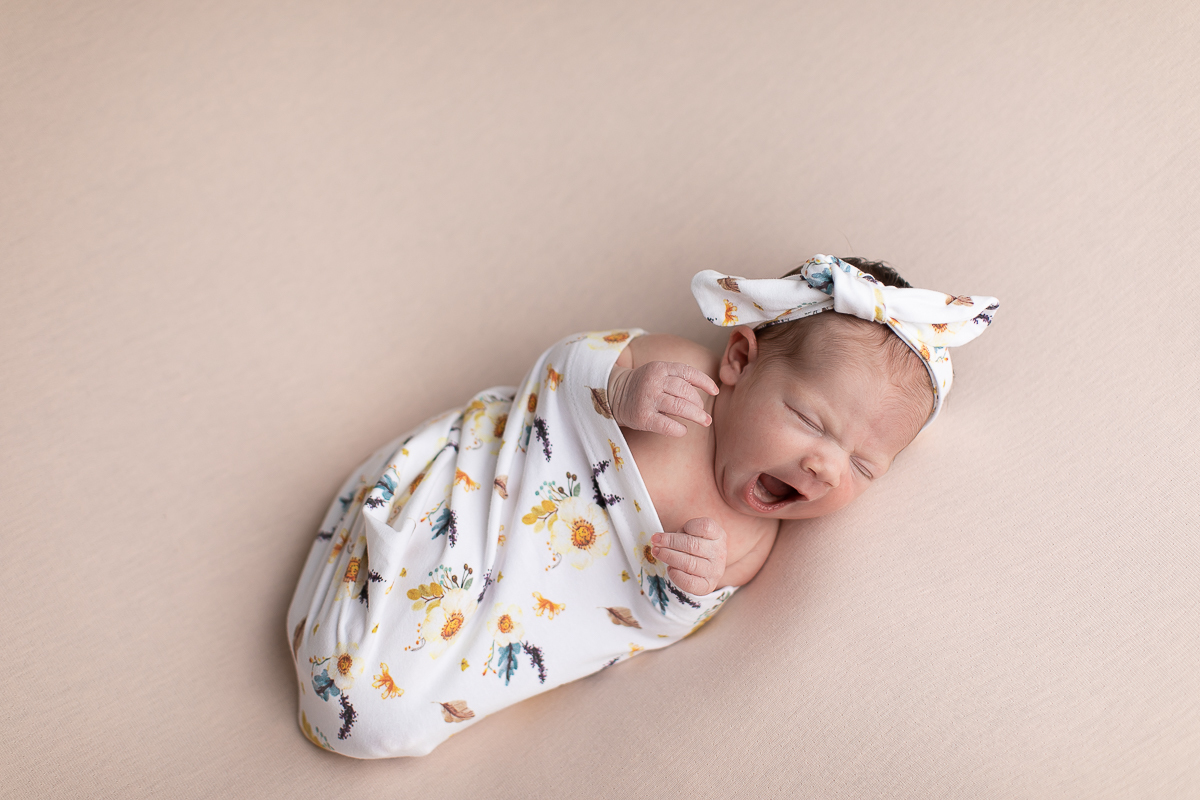 Ensaio newborn da sophia no estúdio gustavo sousa fotografia em curitiba produção simples e clean bebe espreguiçando-se e bocejando. Tecido estampado cor predominante bege  com lacinho do mesmo tecido. 
