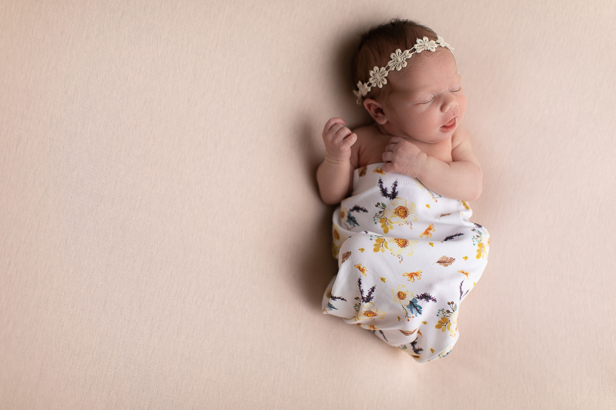Ensaio newborn da sophia no estúdio gustavo sousa fotografia em curitiba produção simples e clean bebe mexendo os bracinhos com olhos fechados.   Tecido estampado cor predominante bege com headband de flor. 
