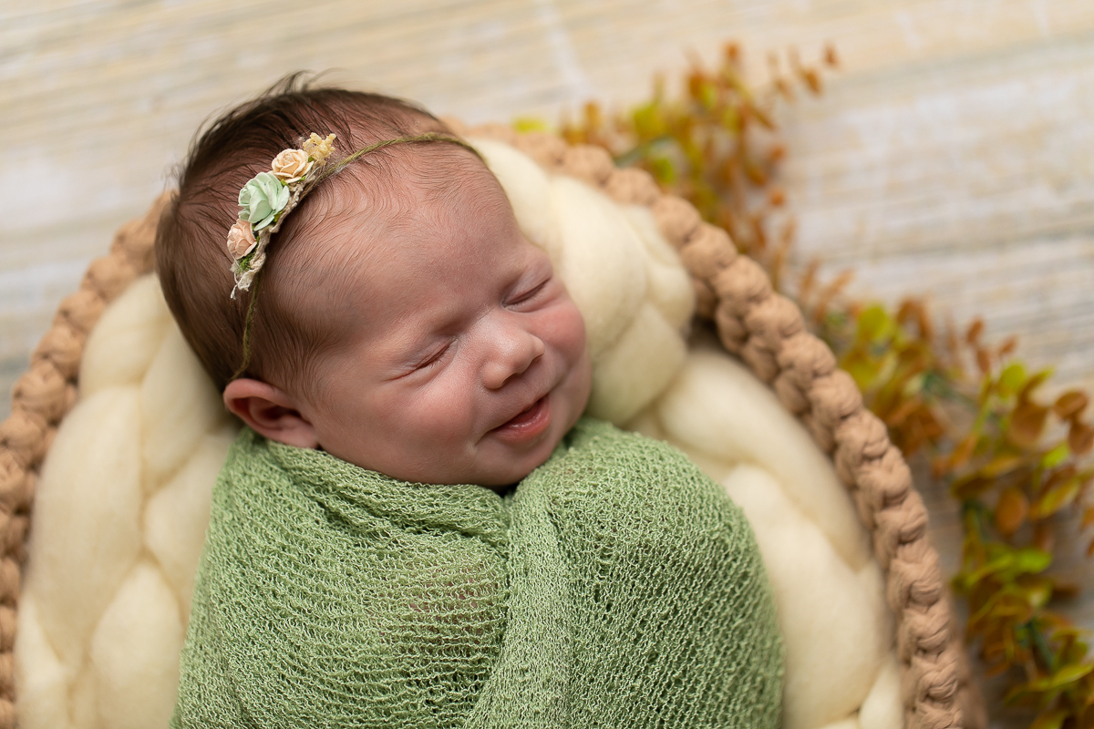 Ensaio newborn da sophia no estúdio gustavo sousa fotografia em curitiba produção simples e clean bebê sorrindo. Bebê enrolado em tecido wrap cor verde mais headband tirinha do cabelo e cesto prop com lã merino. 
 
