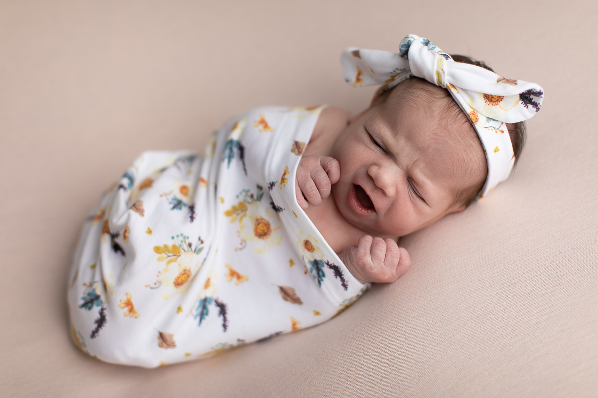 Ensaio newborn da sophia no estúdio gustavo sousa fotografia em curitiba produção simples e clean bebe espreguiçando-se e bocejando. Tecido estampado cor predominante bege  com lacinho do mesmo tecido. 