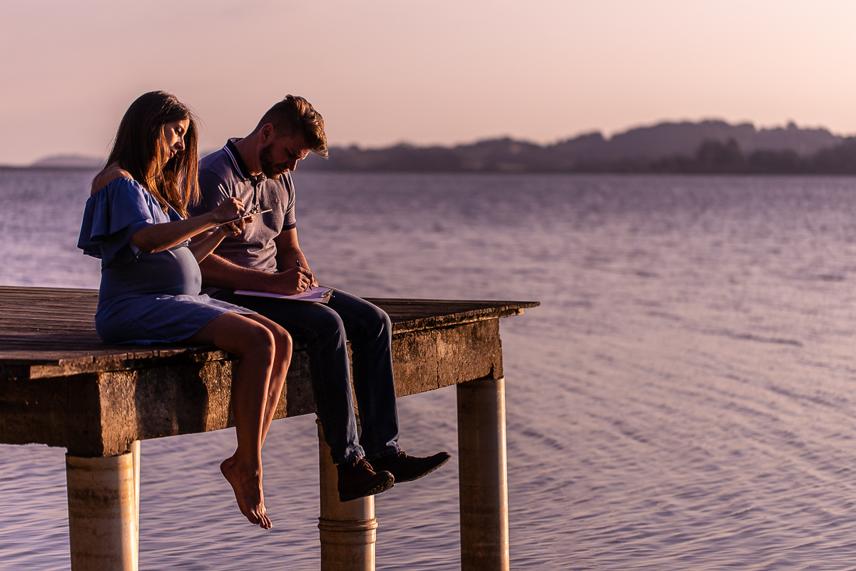 ensaio e book gestante feita por Gustavo Sousa fotografia em Curitiba. Casal Juntos no trapiche do lago fotografia ensaio gestante no por do sol feita pelo gustavo sousa. No Laggus Residencia Laggus. No trapiche  escrevendo carta