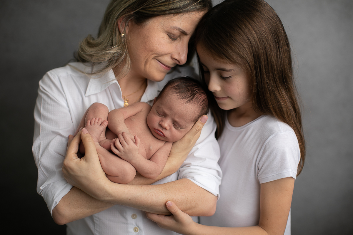 gustavo sousa fotografia ensaio newborn curitiba. mãe e pai segurando o bebê. Mãe e filha em fundo cinza.