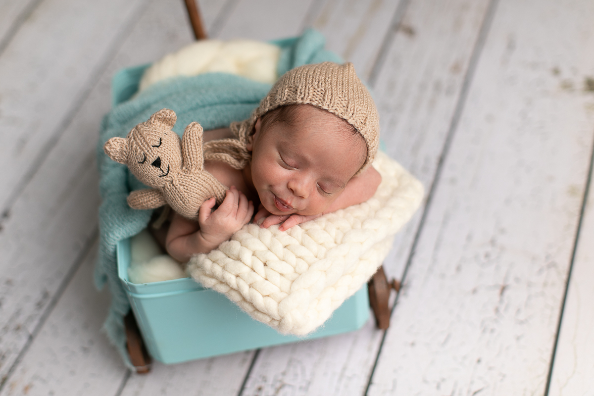 gustavo sousa fotografia ensaio newborn curitiba. Pose do bracinho segurando urso de pelúcia. Fundo fotográfico cinza dentro de carrinho