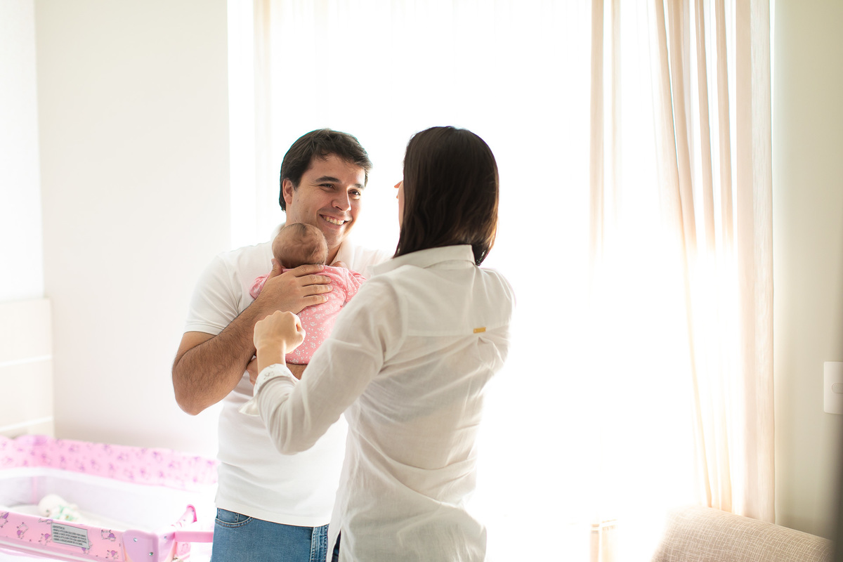 Gustavo Sousa estúdio de fotografia em Maringá-PR. Ensaio e book fotográfico newborn lifestyle e família. Foto em família, pai sorrindo com bebê no colo e mãe de costas.