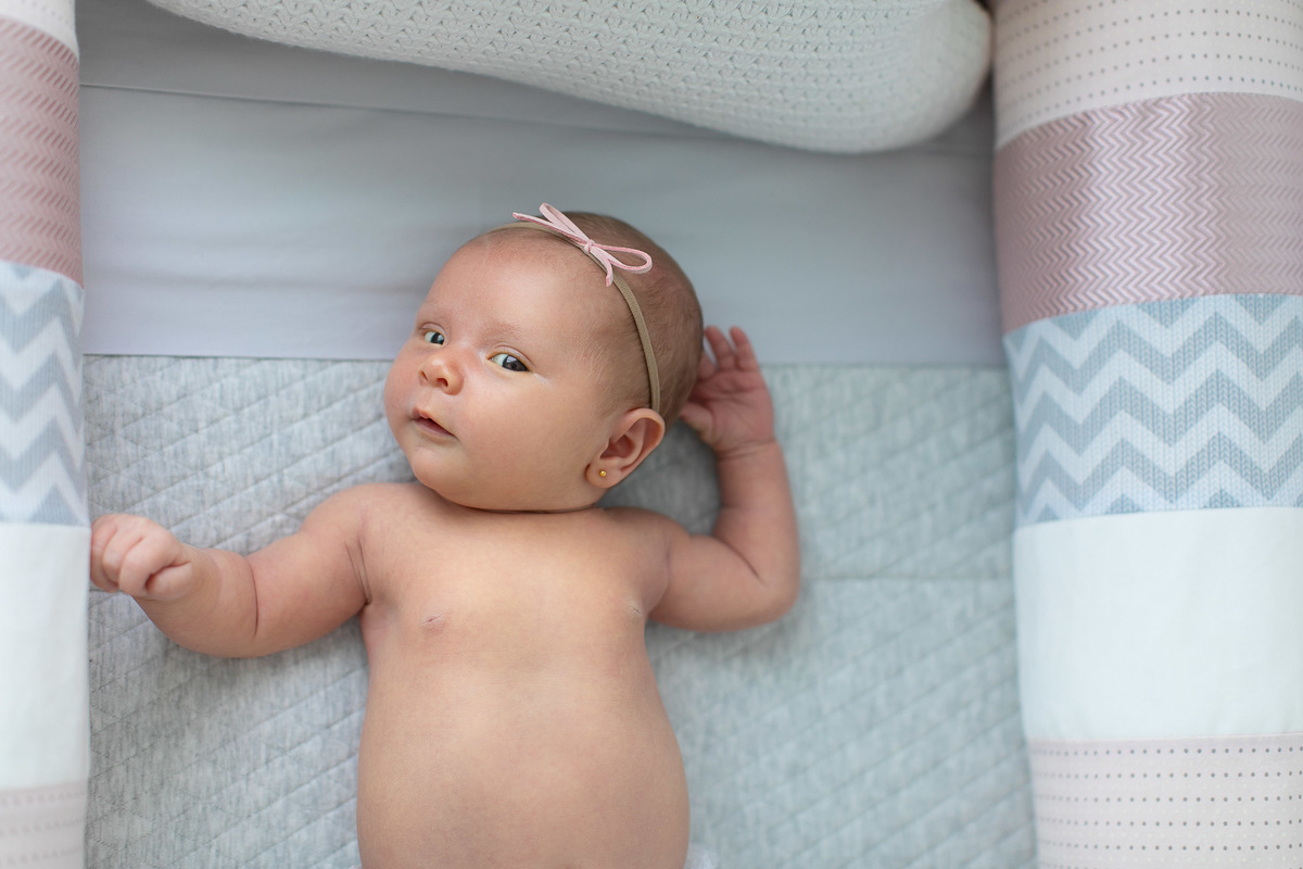 Gustavo Sousa estúdio de fotografia em Maringá-PR. Ensaio e book fotográfico newborn lifestyle e família. Foto de bebê no berço com laço na cabeça.