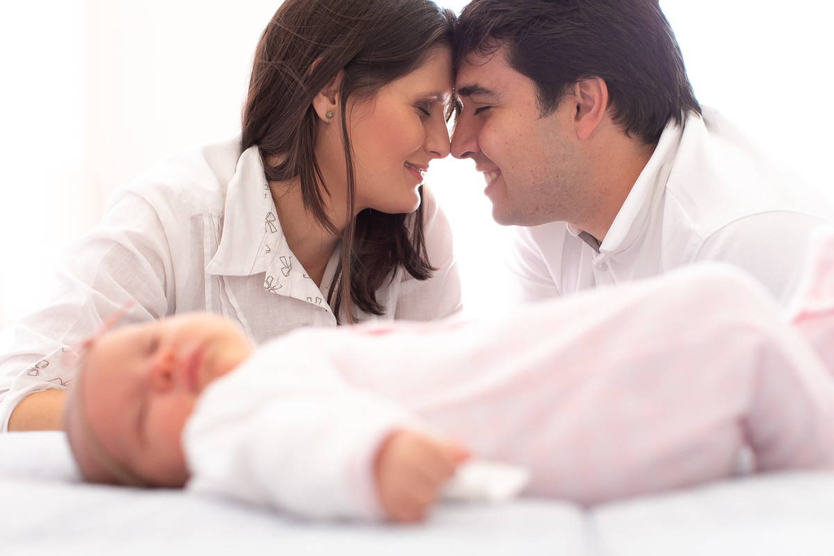 Gustavo Sousa estúdio de fotografia em Maringá-PR. Ensaio e book fotográfico newborn lifestyle e família. Foto em família, pais sorrindo e bebe dormindo na cama.
