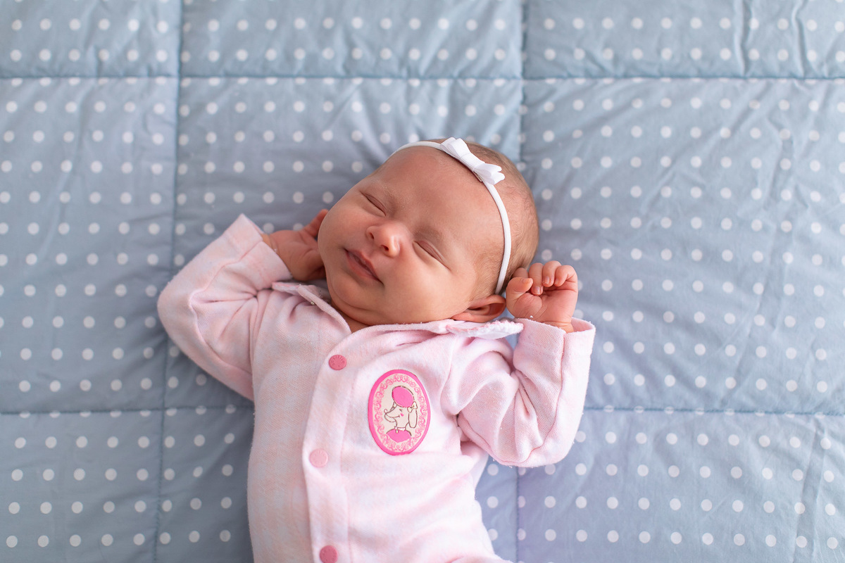 Gustavo Sousa estúdio de fotografia em Maringá-PR. Ensaio e book fotográfico newborn lifestyle e família. Foto de bebê espreguiçando com fundo azul com bolinhas.