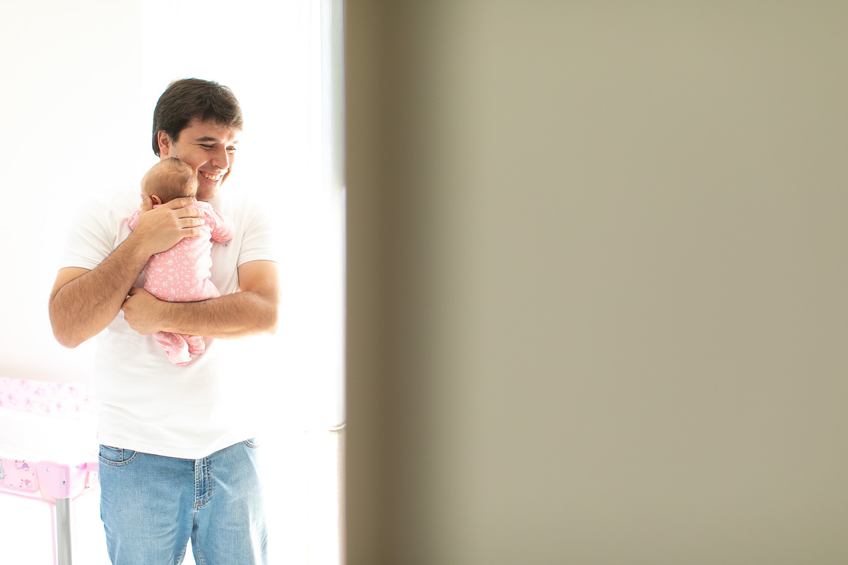 Gustavo Sousa estúdio de fotografia em Maringá-PR. Ensaio e book fotográfico newborn lifestyle e família. Foto do pai sorrindo com bebê no colo.