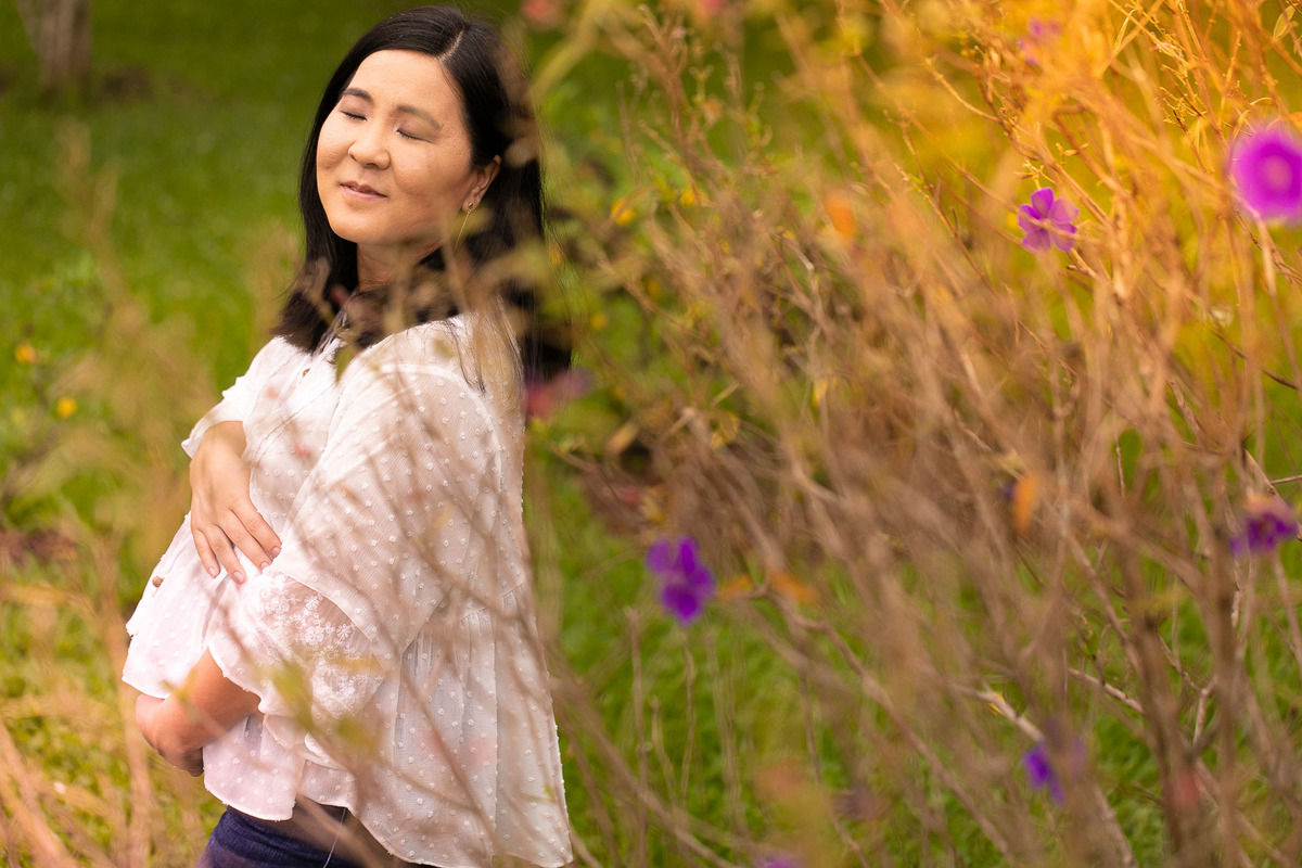 Gustavo Sousa estúdio de fotografia em Maringá-PR. Ensaio e book fotográfico gestante. Foto gestante segurando a barriga com os olhos fechados, arvore com flores roxas.