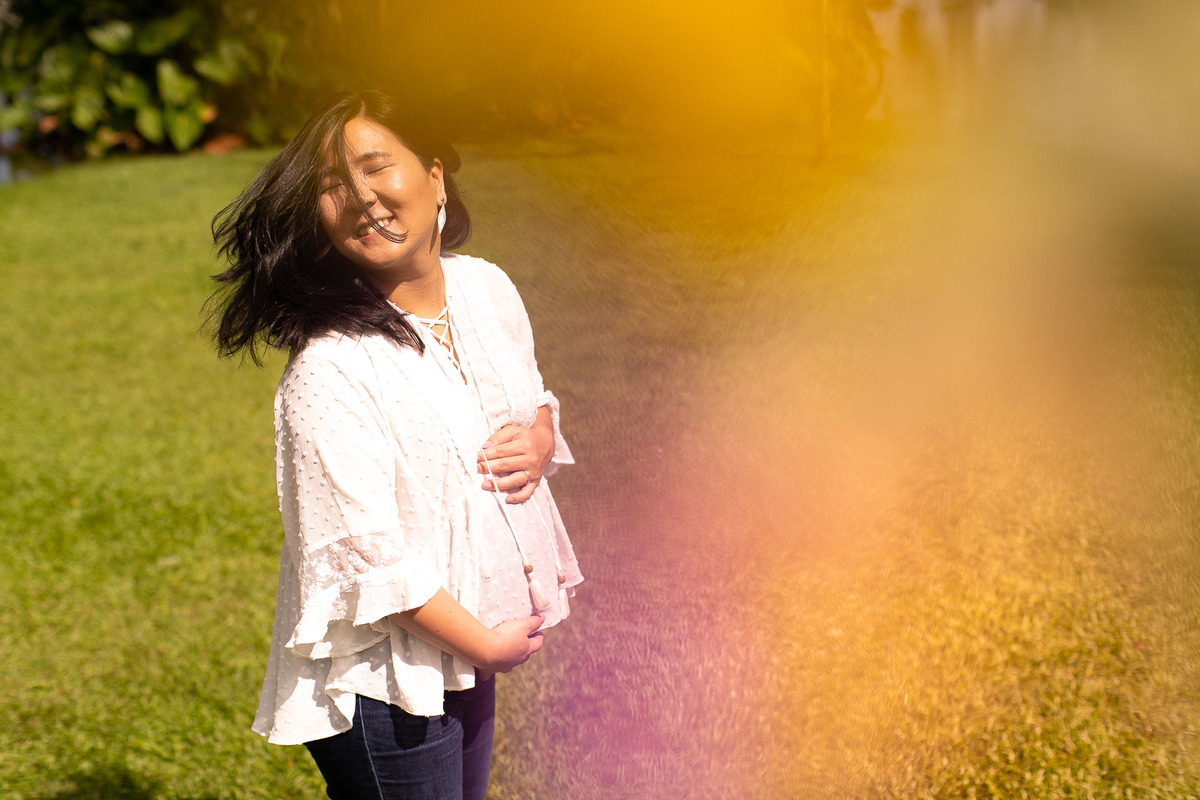Gustavo Sousa estúdio de fotografia em Maringá-PR. Ensaio e book fotográfico gestante. Foto gestante sorrindo e segurando a barriga com os olhos fechados e balançando o cabelo.