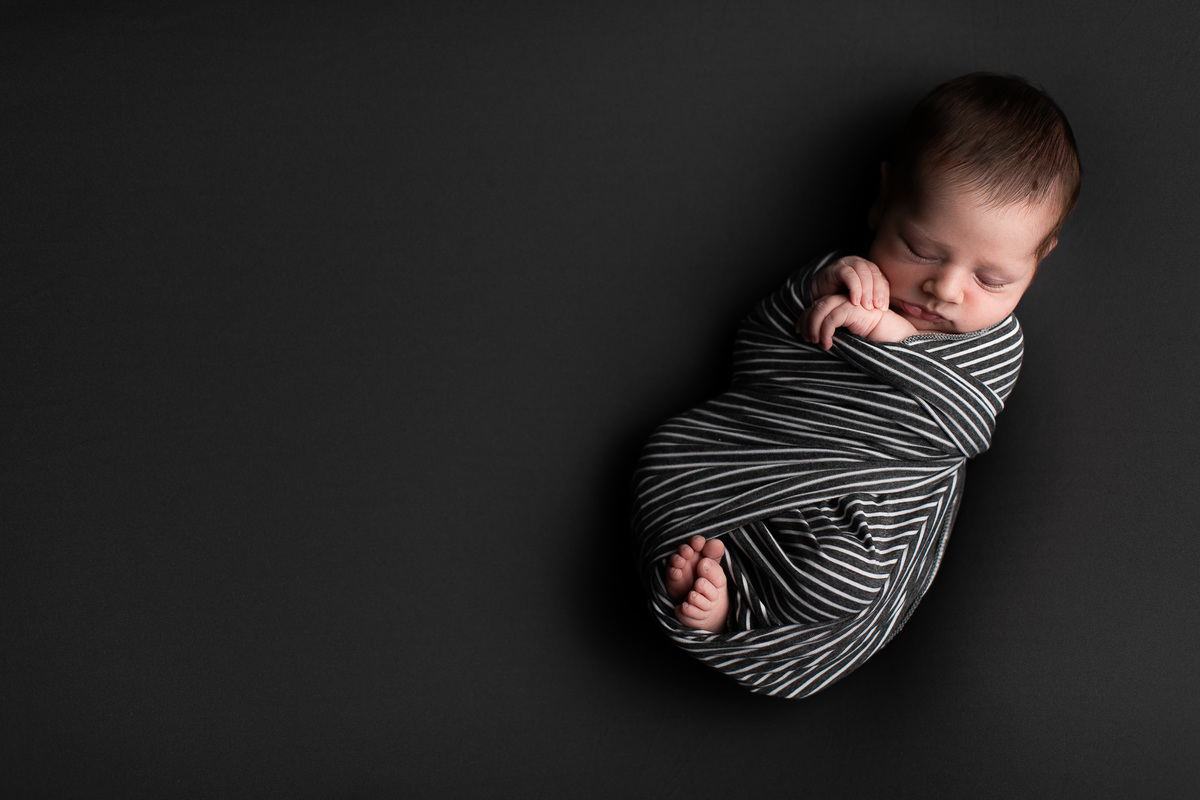 Gustavo Sousa estúdio de fotografia em Maringá-PR. Ensaio e book fotográfico newborn.  Foto bebê enrolado em tecido wrap listrado com pés e mãos a mostra.