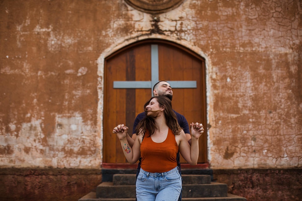Capela Sagrada Família - Ruínas - em Mandaguari, região de Maringá. Casal vestidos de preto em frente a porta da igreja. Foto por Gustavo Sousa Fotografia. Casal posando na frente da porta da igreja