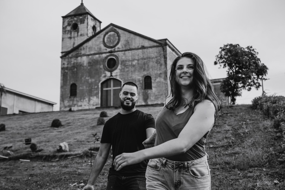 Capela Sagrada Família - Ruínas - em Mandaguari, região de Maringá. Casal vestidos de preto em frente a porta da igreja. Foto por Gustavo Sousa Fotografia. casal correndo na frente da igreja