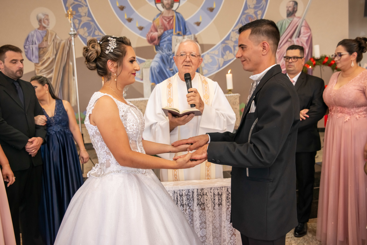 noivos de mãos dadas no alta, padrinhos e padre ao fundo