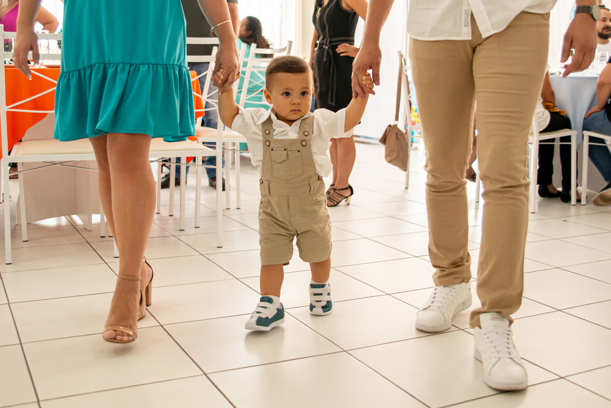 menino de um ano caminhando de mãos dadas com os pais
