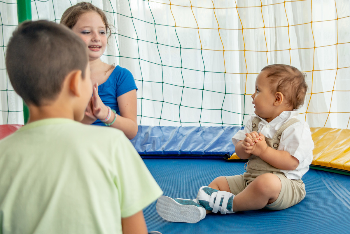 menino de um ano brincando em cama elástica, sorrindo, com outras crianças