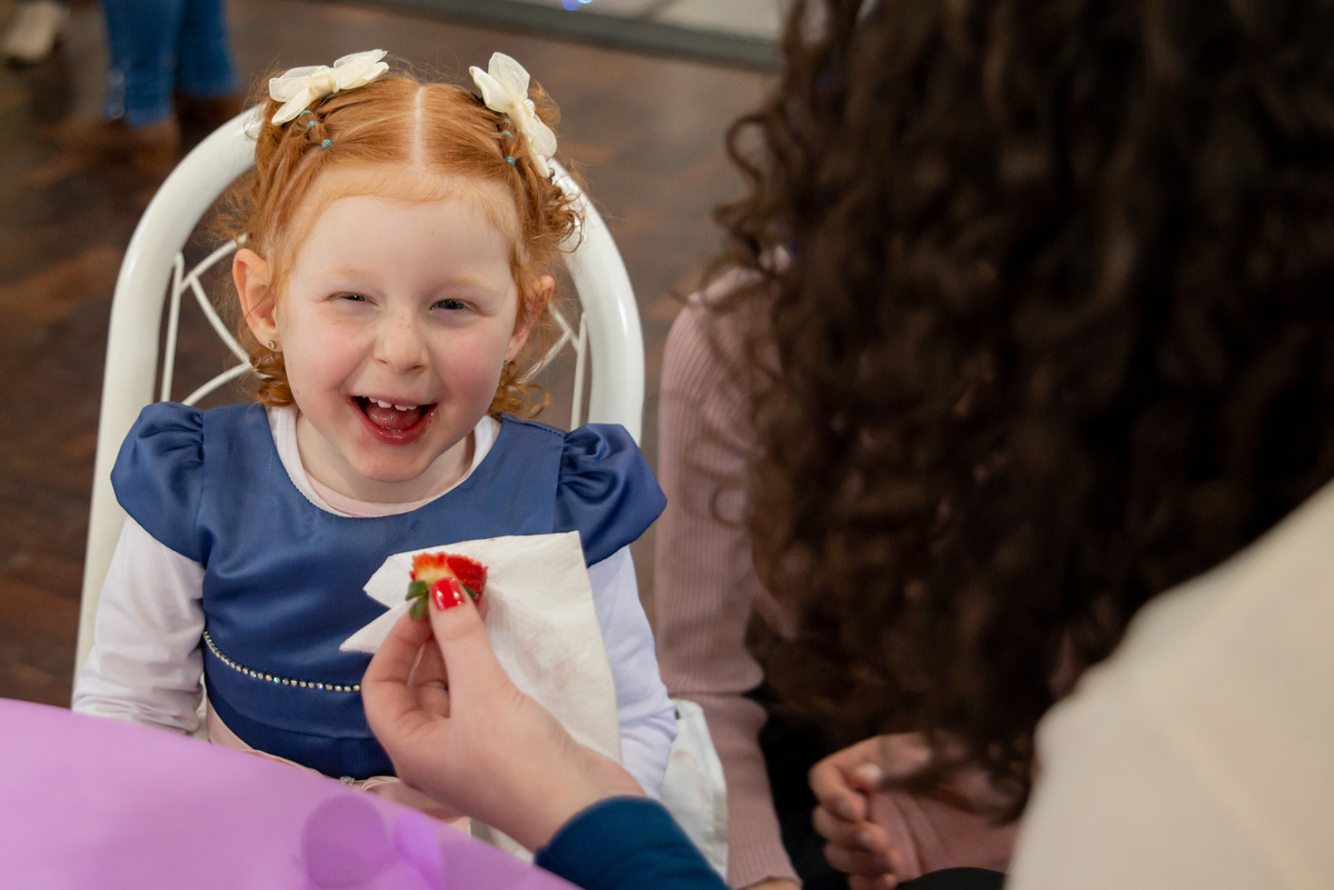 menina ruiva de 3 anos em sua festa de aniversário infantil sorrindo comendo moranguinho