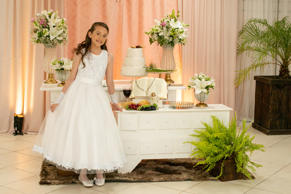 menina com vestido de primeira comunhão eucaristia em frente à decoração
