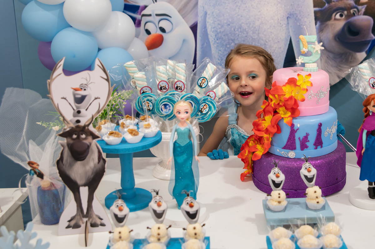 festa de aniversário infantil - aniversariante vestida de Elza - na mesa principal da decoração da Frozen