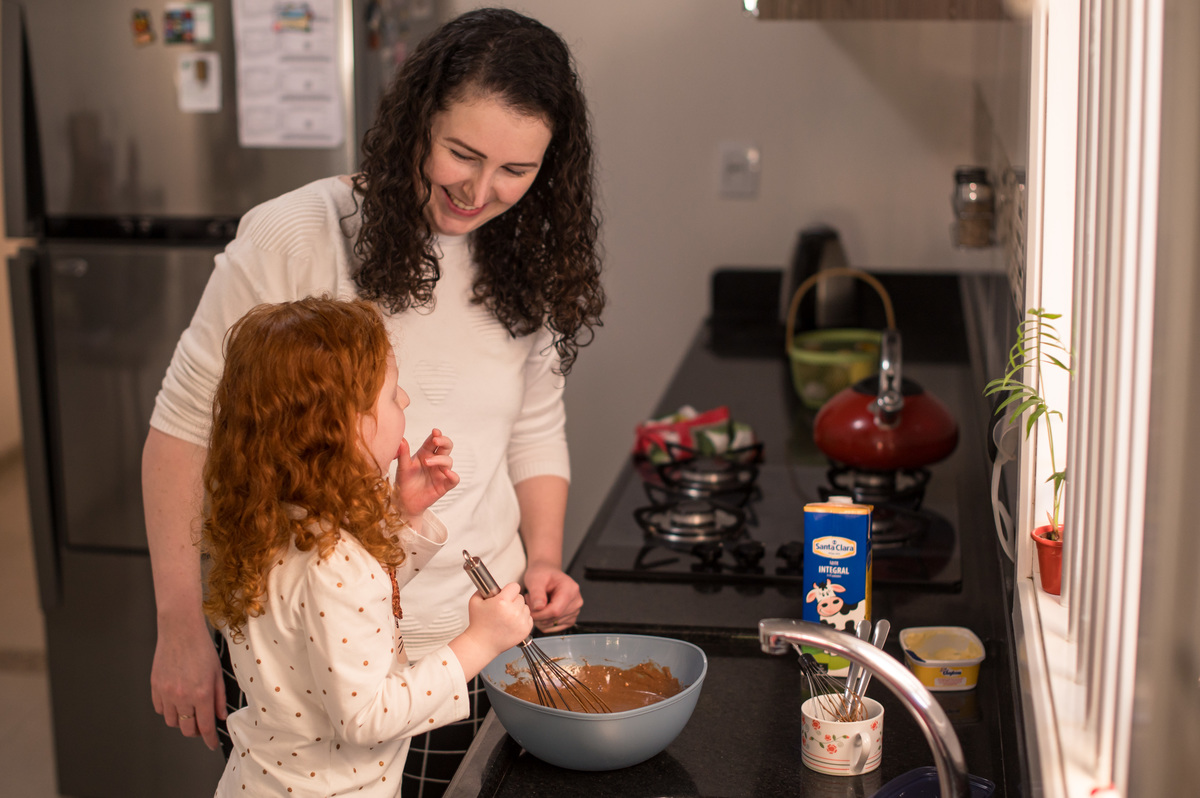 Ensaio de família em casa - menina ruiva fazendo bolo com a mãe