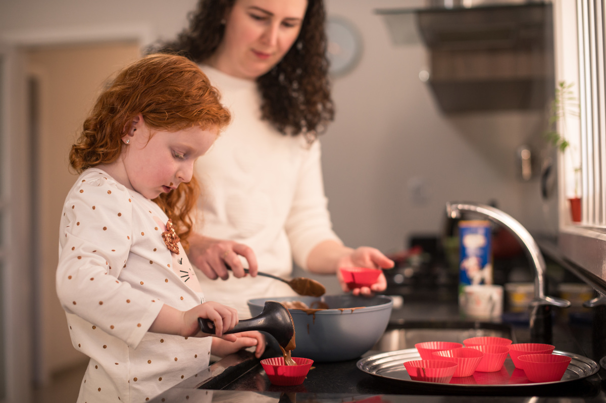 Ensaio de família em casa - menina ruiva fazendo bolinho com a mãe
