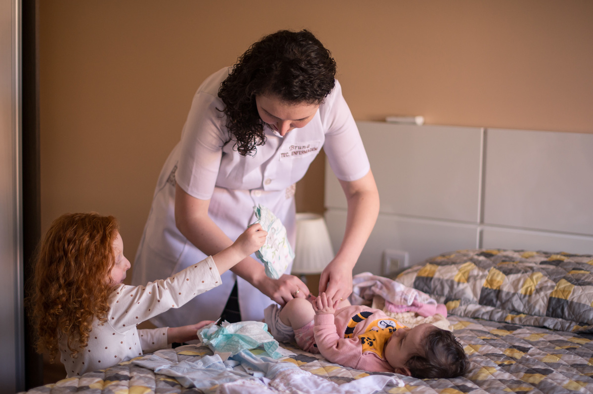 Ensaio de família em casa - filha ajudando a mãe a trocar a fralda