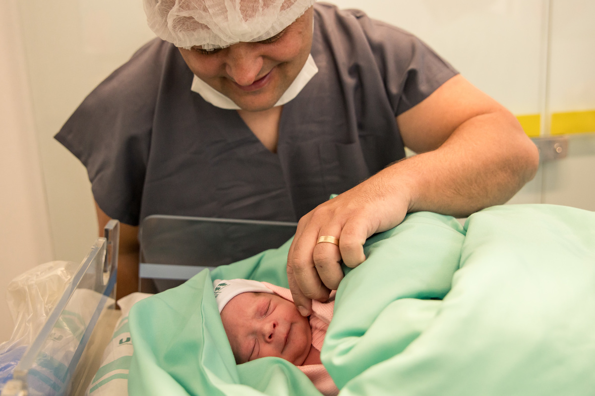 foto de nascimento, bebê parece sorrir ganhando carinho do pai