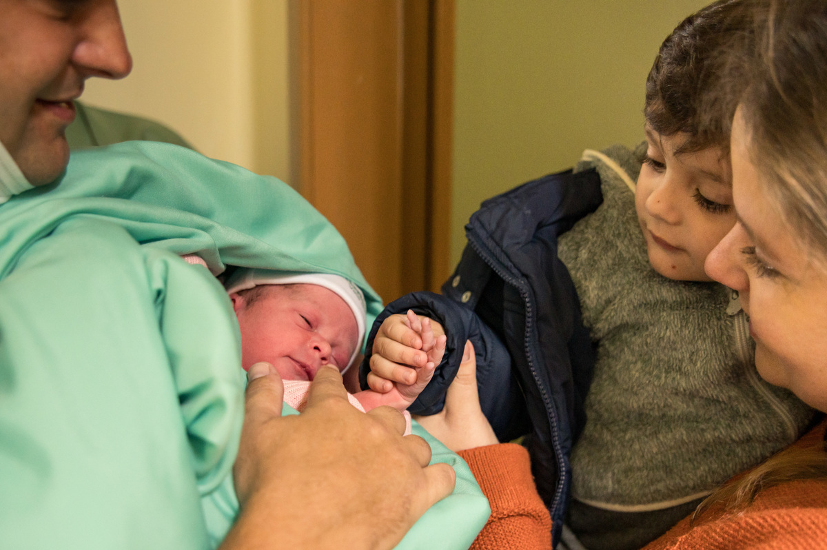 irmão pegando na mão da bebê recém nascida pela primeira vez