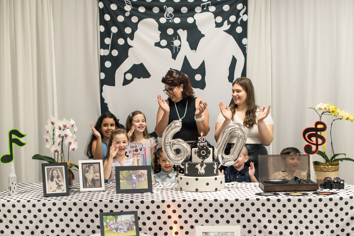 Hora do parabéns na mesa decorada anos 60, aniversariante com os netos