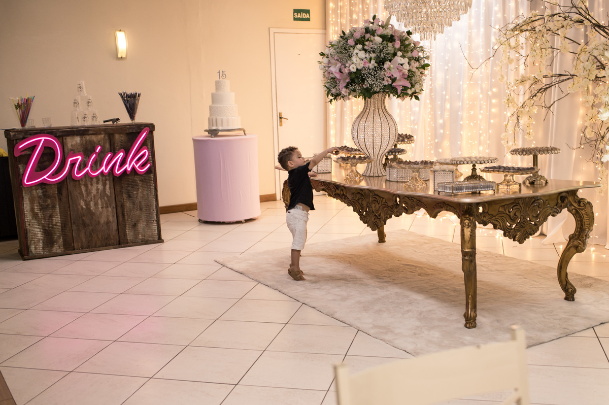 criança roubando docinhos na mesa decorada da festa de 15 anos