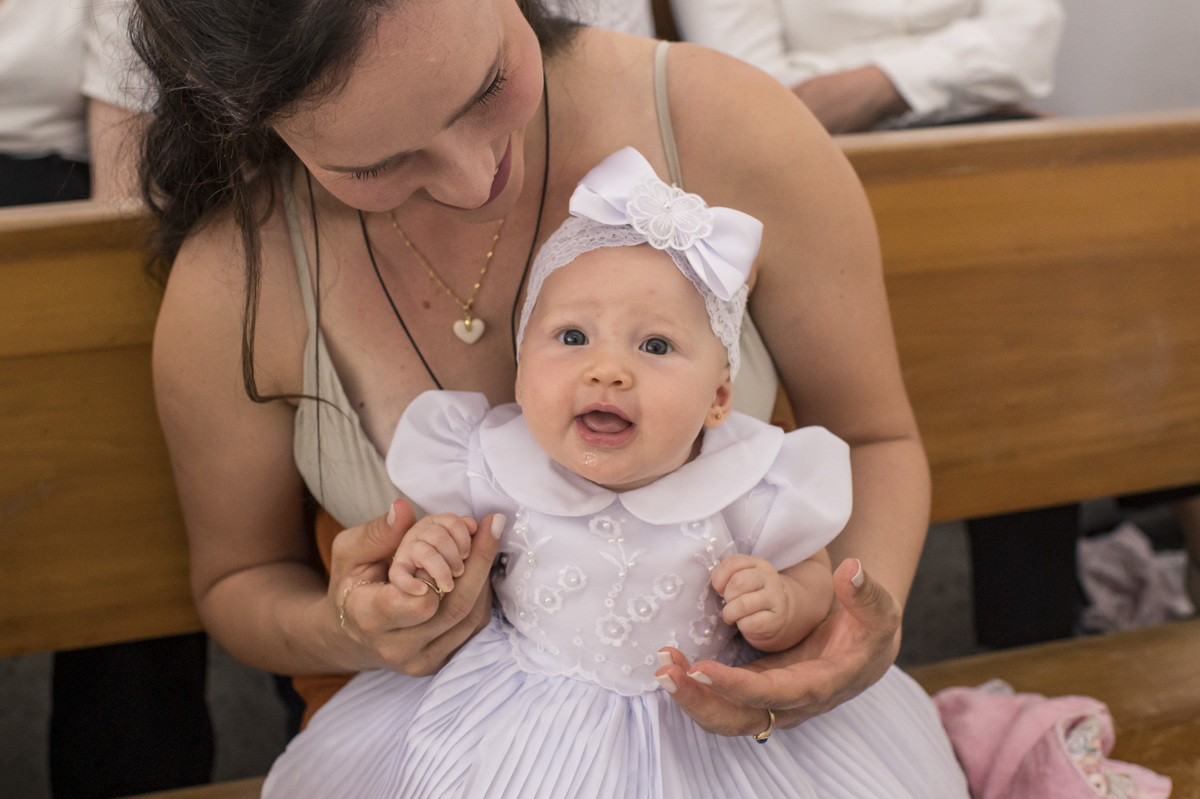 criança sorrindo no colo da mãe no dia do seu batizado